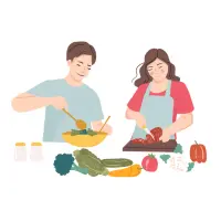 A woman is wearing an apron and holding a spatula. She is reading a recipe book in the kitchen with vegetables, eggs, and cheese on the counter.